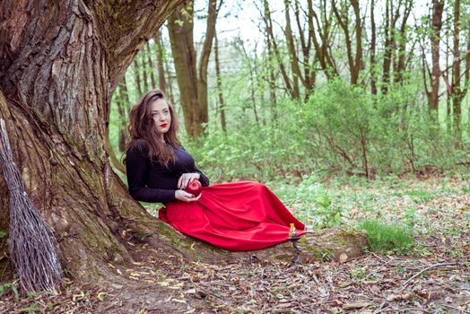 mystical witch woman sitting under a old tree in the forest