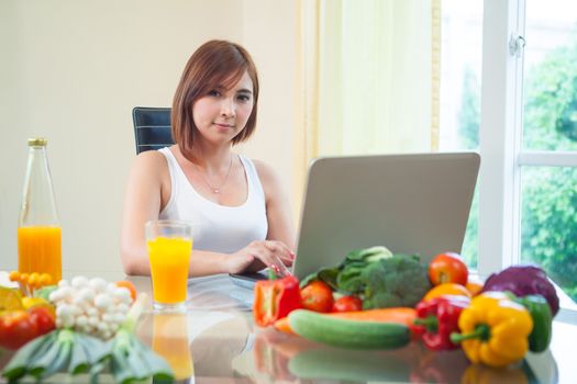 Young asian woman drinking orange juice and using internet at home