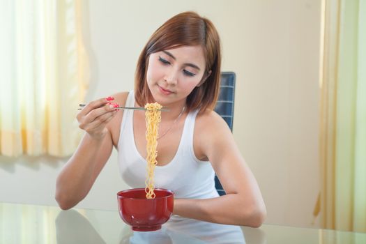 Young Asian girl eating ramen noodles using chopsticks