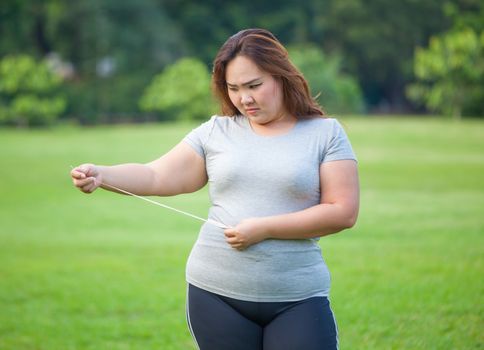 Happy fat asian woman measuring her stomach in the park