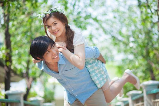 Young asian man giving a piggy back to his girlfriend in the park