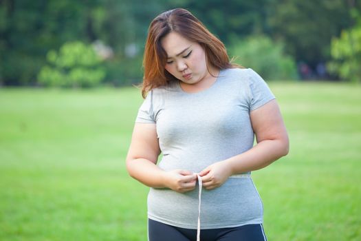 Happy fat asian woman measuring her stomach in the park