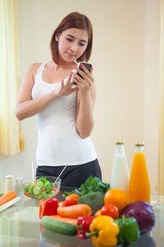 Young asian woman In Kitchen Following Recipe On Mobile phone