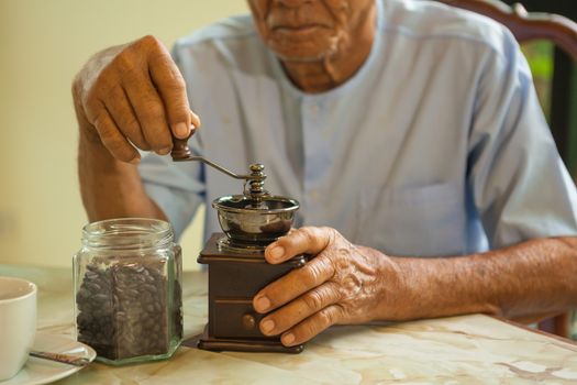 Asian senior man with vintage coffee grinder and coffee beans