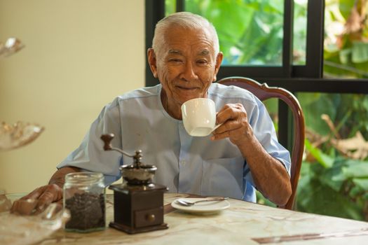 Asian senior man with vintage coffee grinder and coffee beans