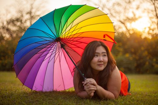Happy fatty asian woman with umbrella outdoor in a park