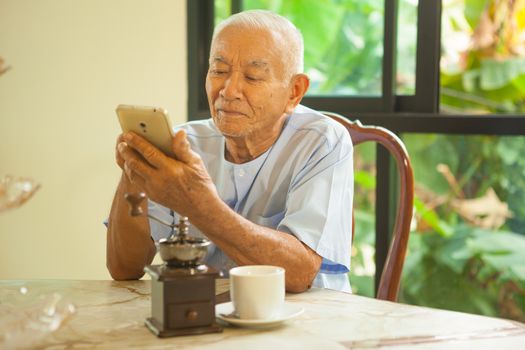 Happy asian senior man using the mobile phone in home