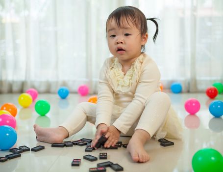 Cute little asian girl playing with black domino in the house