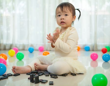 Cute little asian girl playing with black domino in the house