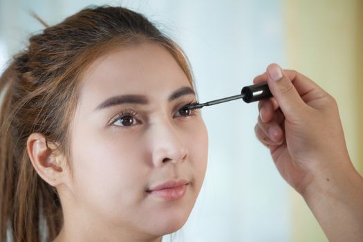 Young asian woman applying mascara on her long eyelashes