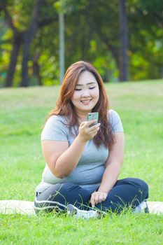 Happy fatty asian woman using mobile phone outdoor in a park