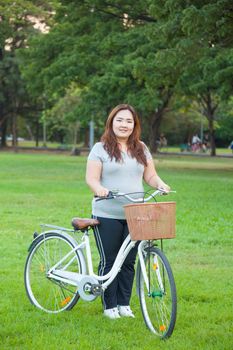 Happy fatty asian woman posing with bicycle outdoor in a park