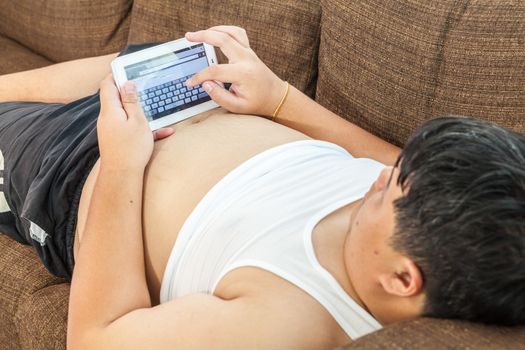 Asian fat man Relaxing in the sofa with the tablet at home