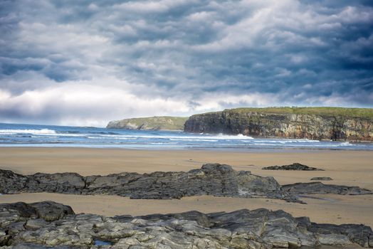 storm clouds with soft waves break on the beach and rocky sand at ballybunion
