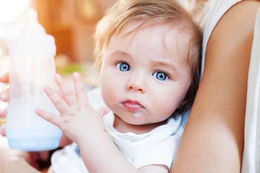 A little baby boy on his mother s lap is looking to camera with big blue eyes and milky mustache, holding a bottle with pacifier.