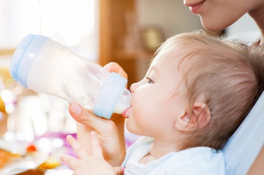 A baby boy is fed with milk from a pacifier bottle by his young mother.