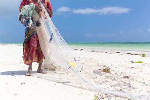 Traditional african local rural fishing on Paje beach, Zanzibar, Tanzania. Traditionally dressed local woman pulling fishing net, catching small fish.