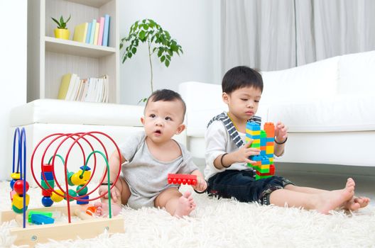 Asian kids sitting on the floor, playing with toy.