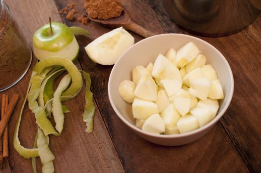 Single partially peeled golden delicious apple beside chopped pieces in bowl on table