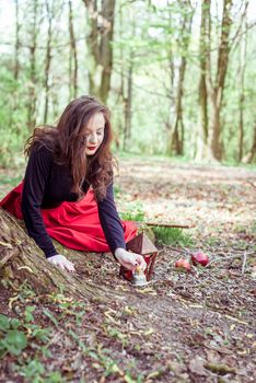 mystical witch woman in red dress lights a candle in the spring forest