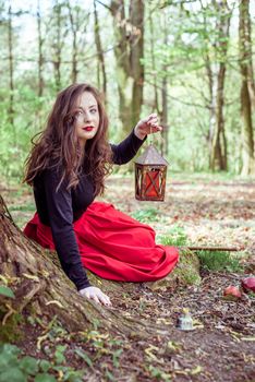 mystical witch woman sitting and holding a lantern in the forest