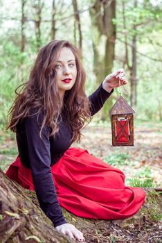 mystical witch woman sitting and holding a lantern in the forest