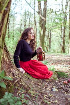 mystical witch woman sitting and holding a lantern in the forest