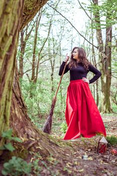 female witch standing with wooden broom in the spring forest