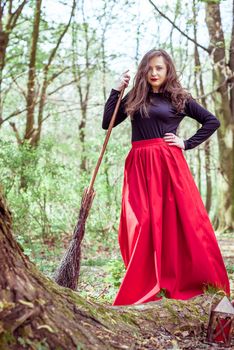 female witch standing with wooden broom in the spring forest