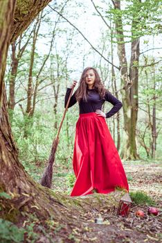 female witch standing with wooden broom in the spring forest