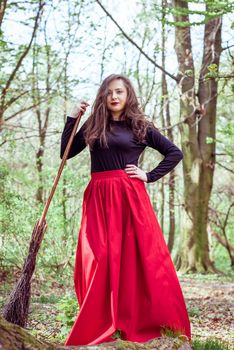 female witch standing with wooden broom in the spring forest