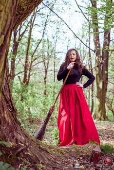 female witch standing with wooden broom in the spring forest