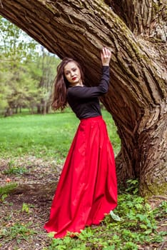 beautiful woman in a red dress standing near a tree in the forest