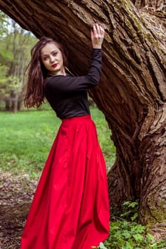 close-up beautiful woman in a red dress standing near a tree in the forest