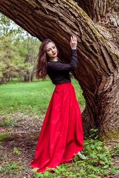 close-up beautiful woman in a red dress standing near a tree in the forest