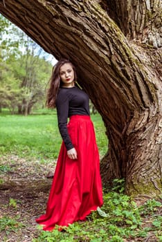 close-up beautiful woman in a red dress standing near a tree in the forest