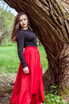 close-up beautiful woman in a red dress standing near a tree in the forest