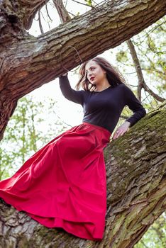 beautiful woman in a red dress sitting on a trunk in the spring forest