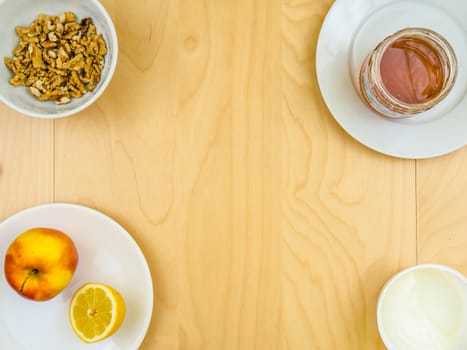 Four ingredients for a healthy and nutritious snack or smoothie, apple lemon fruit, cottage cheese, honey , shelled nuts walnuts, on plates from top view, arranged on wooden table in soft colours with copy space in the middle