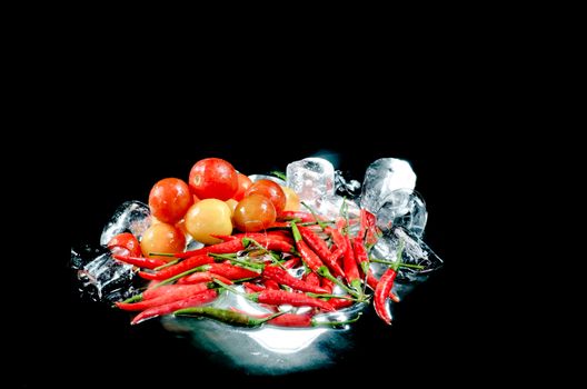 Red hot chilli peppers tomato and ice on the black background.