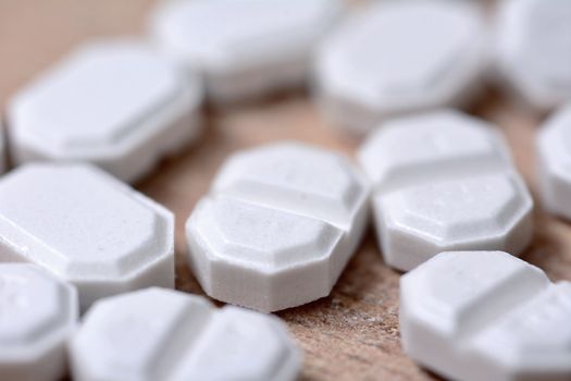 Macro of the white pills on wooden brown background.