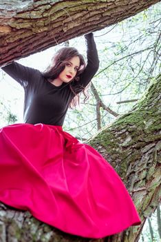 beautiful young woman in a red skirt sitting on a tree trunk in spring forest