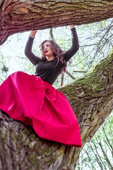 beautiful young woman in a red skirt sitting on a tree trunk in spring forest