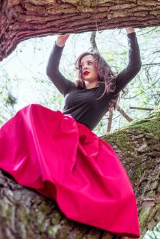 beautiful young woman in a red skirt sitting on a tree trunk in spring forest