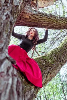 beautiful young woman in a red skirt sitting on a tree trunk in spring forest