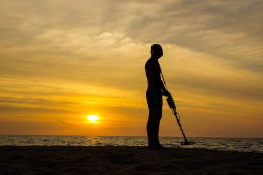 a treasure hunter with Metal detector on sunset on the beach