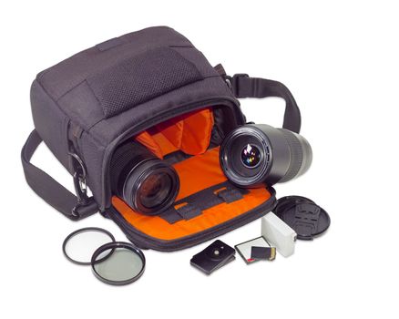 Two different photo lenses in the open camera bag and some other photo accessories beside on a light background
