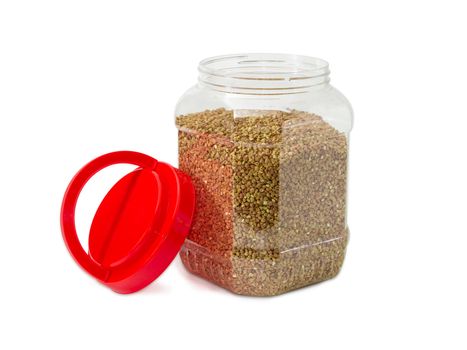 Buckwheat groats peeled from the husk in the transparent plastic container with the open red cover on a light background
