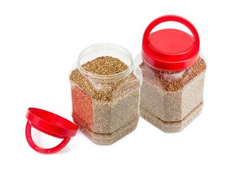 Buckwheat groats peeled from the husk in two transparent plastic containers with the red covers, one of them open on a light background
