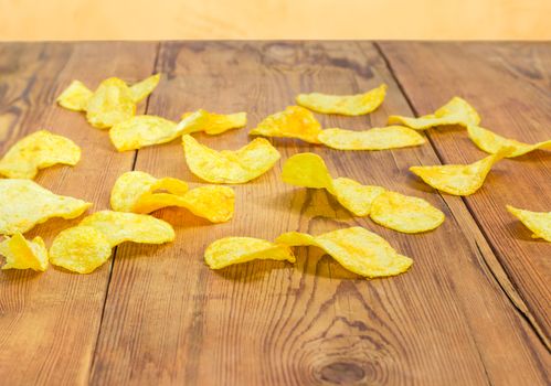 Potato chips scattered on the surface of the old darkened by time wooden planks closeup 
